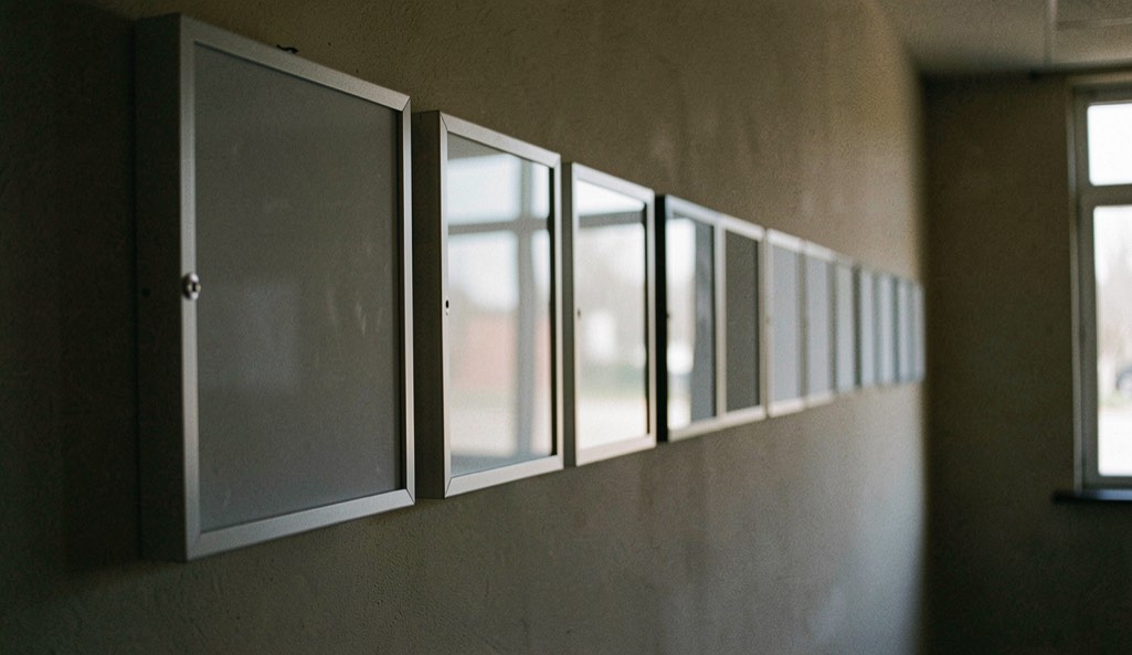 A row of blank light boxes on a wall in a darkened room, their frames catching a faint reflection from a window out of shot